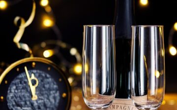 two glasses standing on a table with a black background and a clock in front.